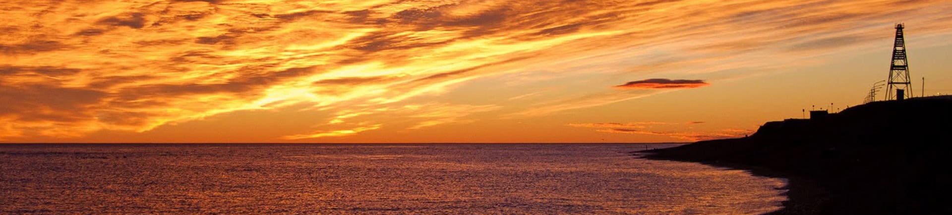 Sunset over the coast with oil rig in the distance, showcasing natural beauty and industrial presenc.