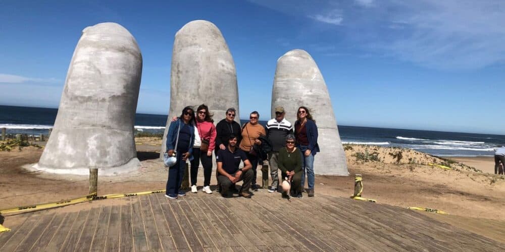 Escultura de dedos gigantes en la playa con grupo de personas en primer plano.