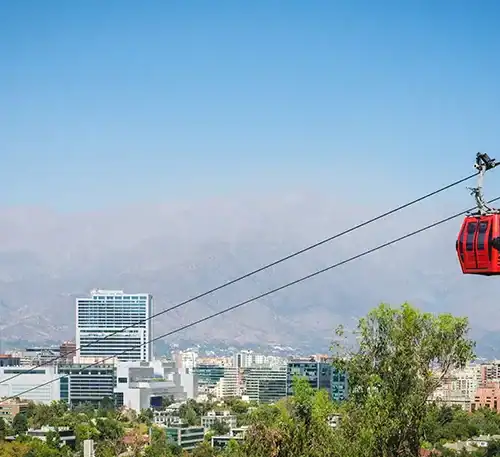 Cable car en la ciudad con rascacielos y montañas de fondo, vista panorámica urbana y natural.