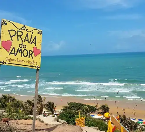 Pancarta en la playa que dice "Praia do Amor" con fondo de mar y arena, en un día soleado.