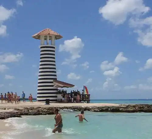 A lighthouse with black and white stripes on a beach under a blue sky.