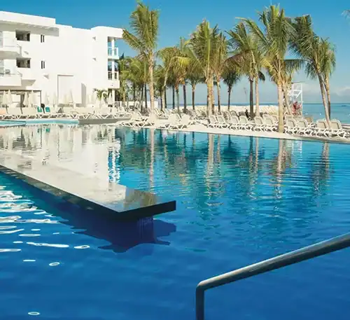 Relaxing pool area with palm trees and ocean view at a tropical resort.