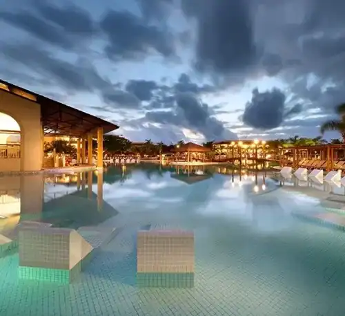 Luxurious outdoor pool area with lounge chairs and tropical surroundings at dusk.