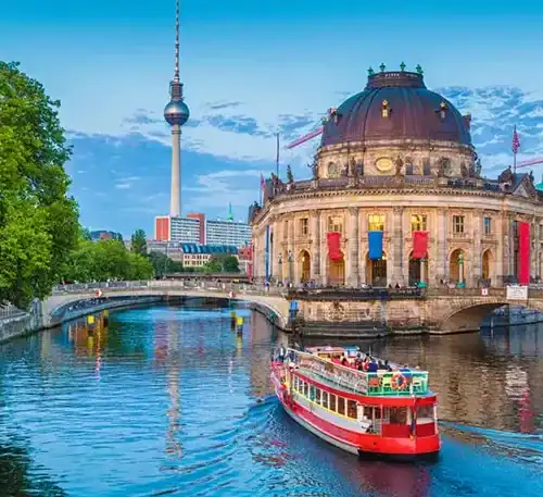Historic building and river in Berlin with TV Tower in background.