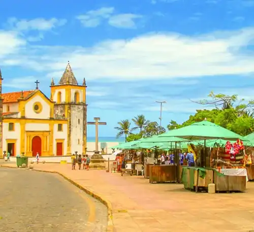 Catedral histórica en un pueblo costero con mercado al aire libre y palmeras bajo cielo azul.