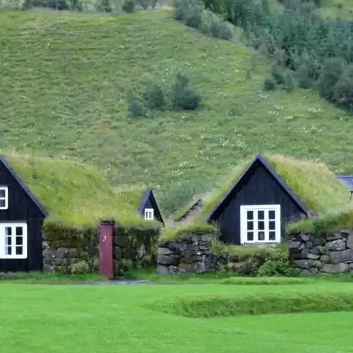 Casas tradicionales con techos de césped en un paisaje verde y montañoso.