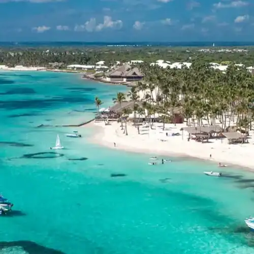 Barco en aguas cristalinas de una playa tropical con palmeras y resorts.
