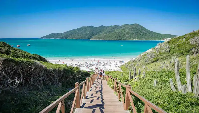 A lush green pathway leading to a pristine beach with turquoise waters and distant mountains.