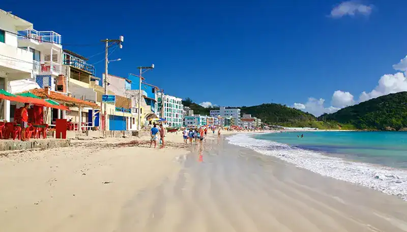 A beach scene with colorful buildings and people enjoying the sunny day.
