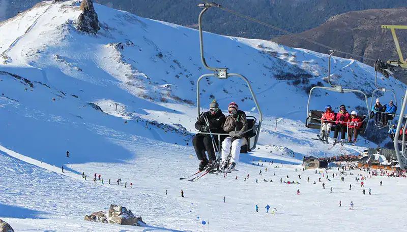 Ski lift with skiers enjoying a snowy mountain landscape in winter.