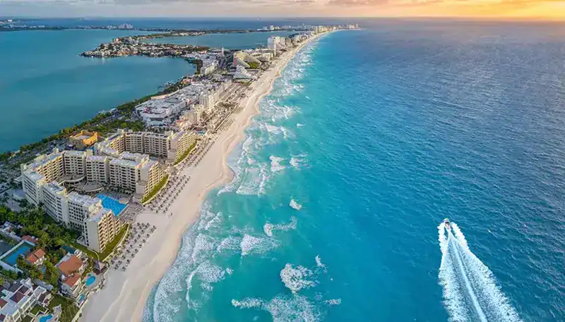 Aerial view of a coastal city with high-rise buildings and a long sandy beach at sunset.