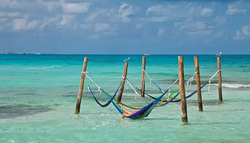 Relaxing hammock between wooden posts over clear turquoise ocean waters.