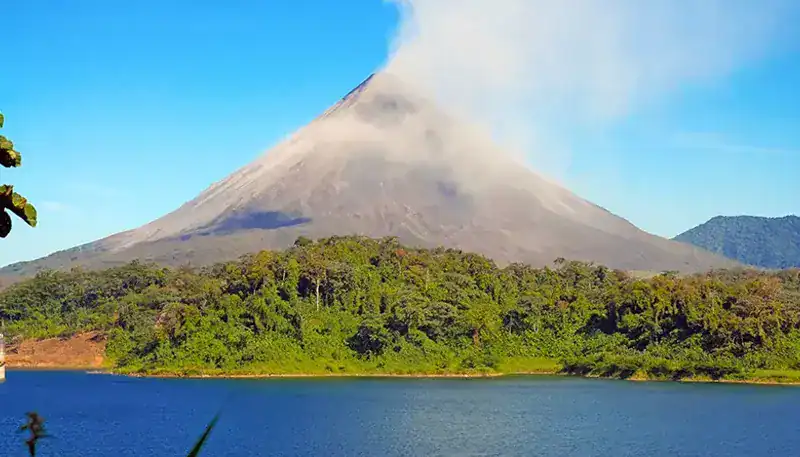 Volcán activo en medio de un paisaje natural con lago y vegetación exuberante.