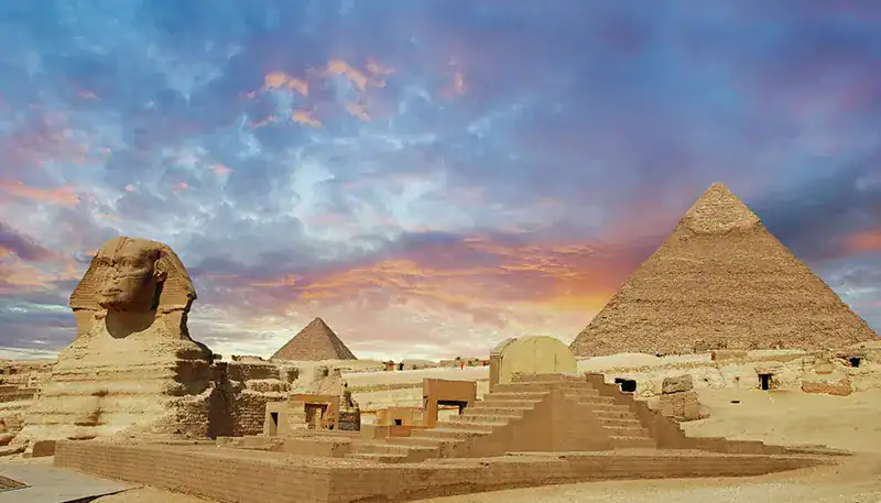 Ancient Egyptian pyramids and Sphinx at sunset, iconic archaeological site in Giza, Egypt.
