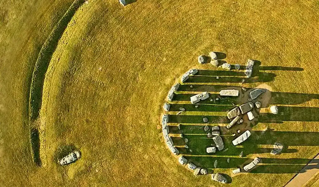 Stone circle with standing stones on grassy field, aerial view.