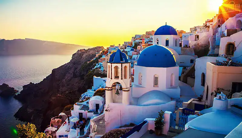 Paisaje de Santorini con casas blancas y cúpulas azules al atardecer.