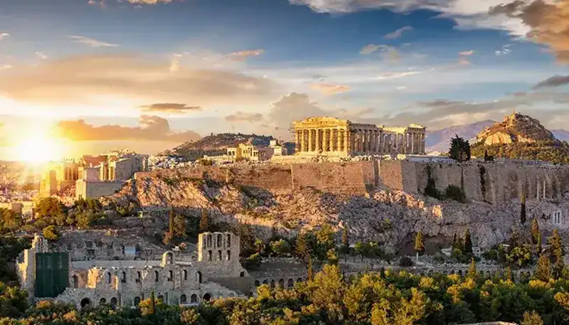 Vista de la Acrópolis de Atenas al atardecer con cielo despejado y nubes dispersas.