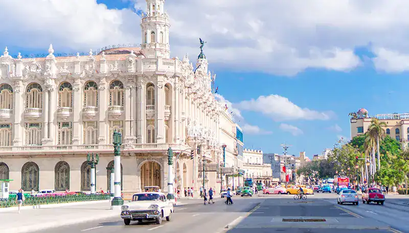 Historic building on a busy city street with cars and pedestrians in Havana, Cuba.
