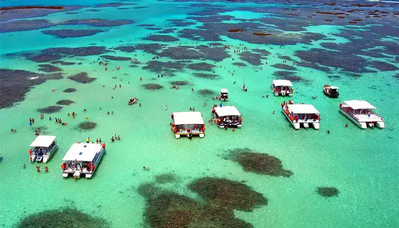 Swimming in clear turquoise waters with boats and people enjoying a tropical beach scene.