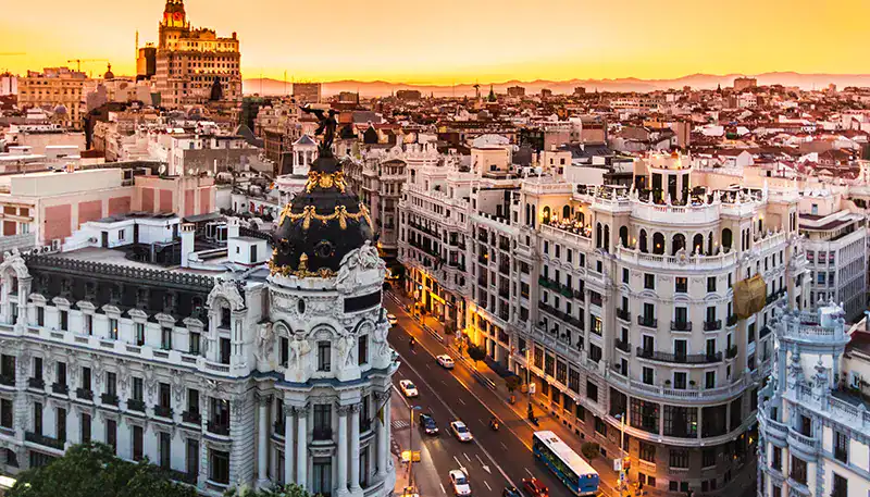 El Kaminante, vista panorámica de Madrid al atardecer con edificios históricos y calles iluminadas.