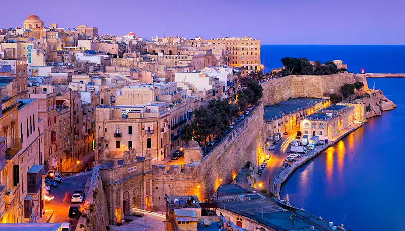 A stunning view of a historic coastal city with colorful buildings and a calm harbor at sunset.
