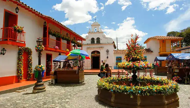 Balcón con flores y puestos en una plaza colonial en un día soleado en El Kaminante.