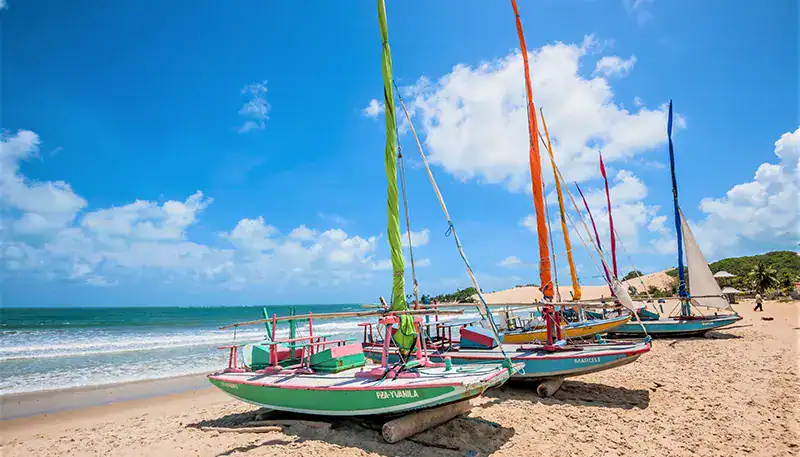 Barcos de vela en la playa con cielo azul y nubes en el fondo.