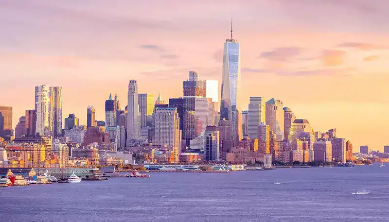New York City skyline at sunset with One World Trade Center prominently visible.