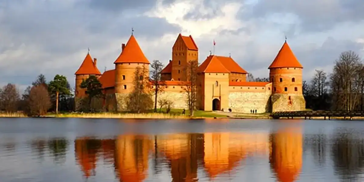 Castillo medieval en un lago con reflejo, arquitectura histórica y paisaje natural en un día nublado.