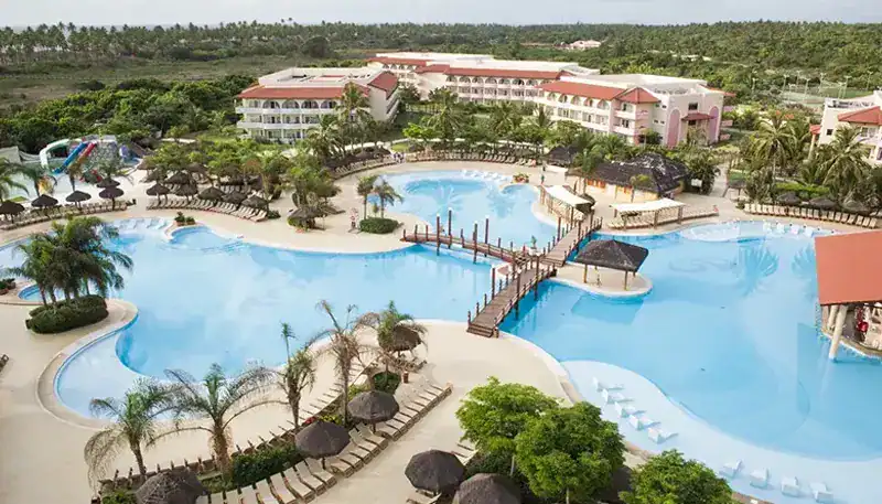 Piscina grande en resort con áreas de descanso y vegetación tropical.