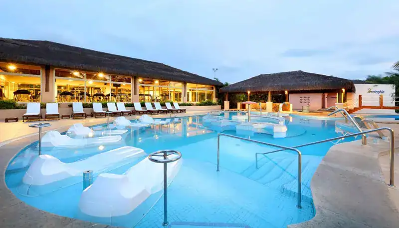 Piscina exterior con zona de descanso y bar en un hotel de lujo en la noche.