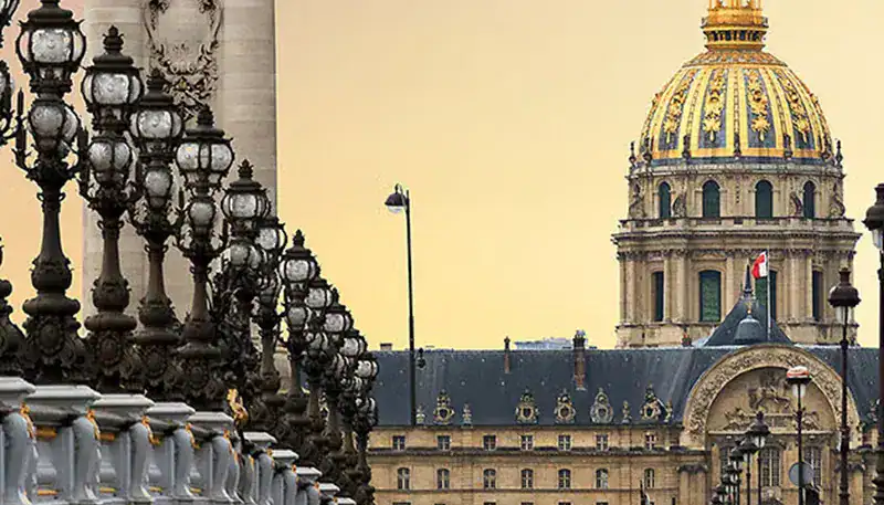 Elegant Parisian architecture with ornate street lamps and historic domed building at sunset.