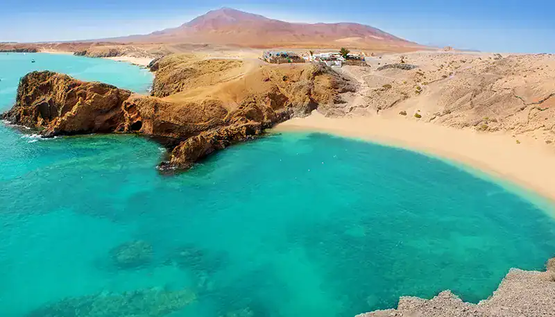 Bañista en playa de aguas cristalinas y arena dorada en un paisaje costero.