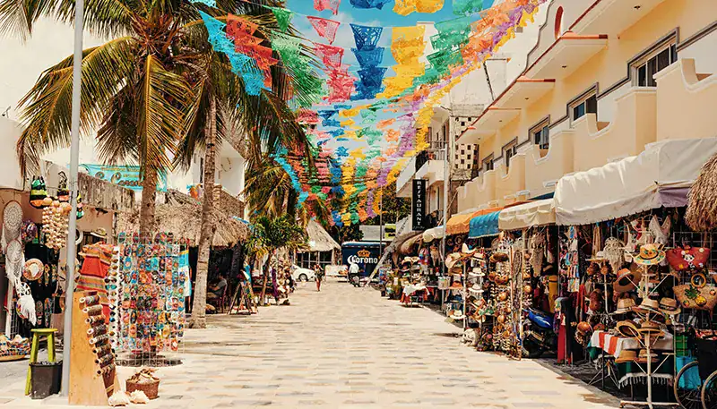 Colorful street market with hanging decorations and souvenir stalls in a sunny coastal town.