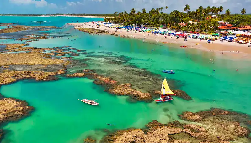 A lush tropical beach with turquoise waters and boats near the shore.