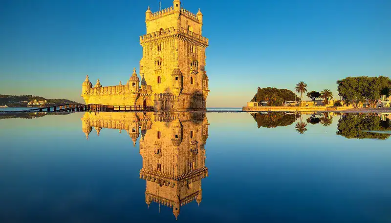 A stunning view of the iconic Belém Tower reflected in the calm waters of the Tagus River at sunset.