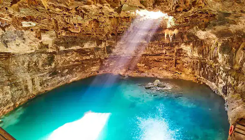 A lush waterfall cascading into a vibrant blue pool in a natural cave setting.