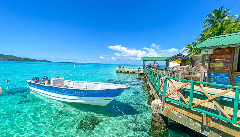 Relaxing tropical beach with clear turquoise water and a wooden pier in the background.
