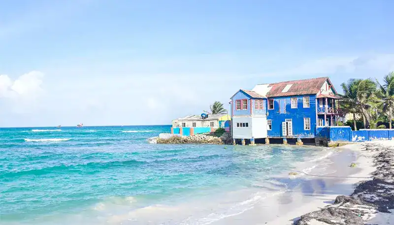 A colorful house by the beach with turquoise waters and a clear sky.