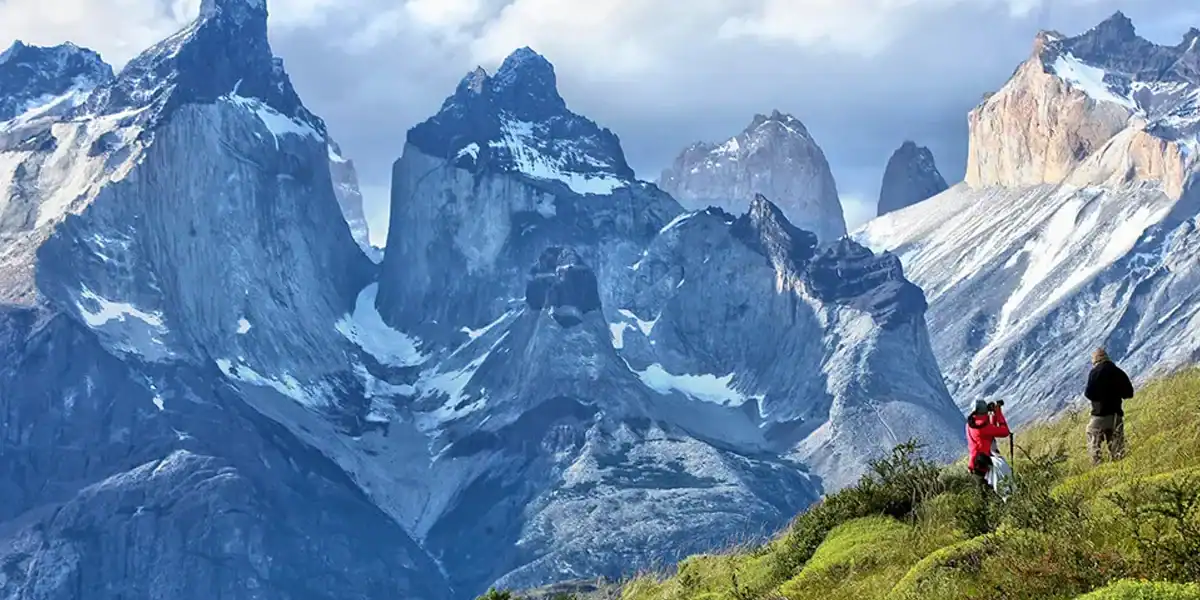 A mountain landscape with hikers in the foreground and rugged peaks in the background.