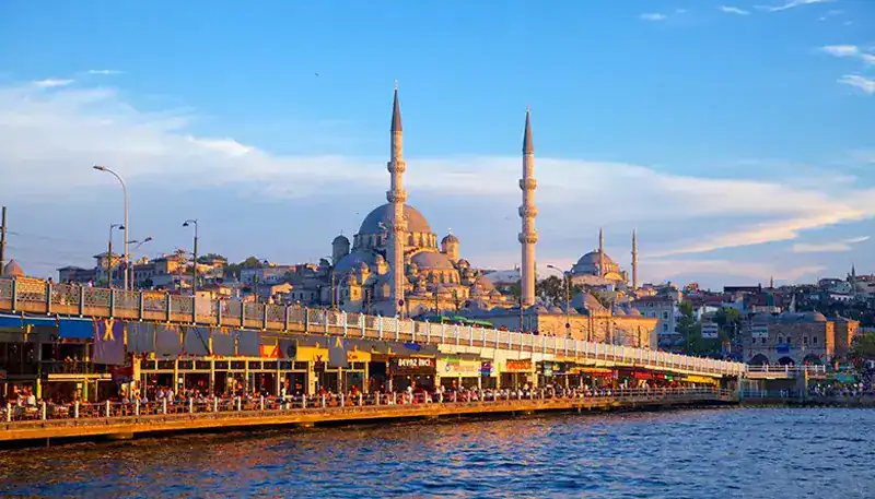 A mosque with two minarets along a waterfront at sunset.