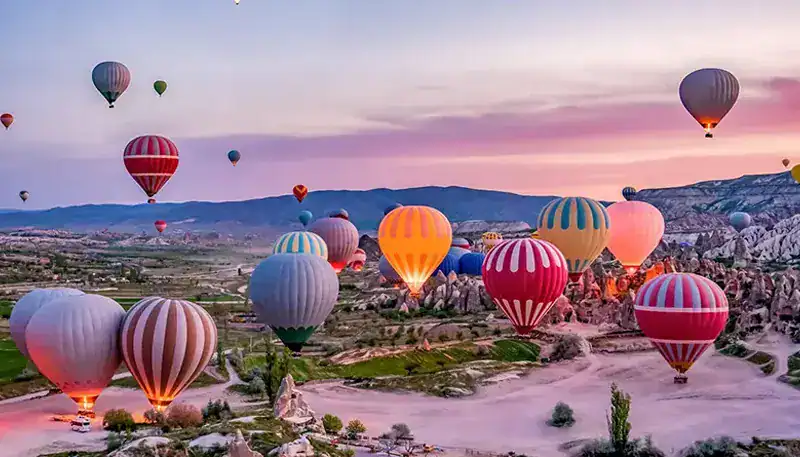 A colorful hot air balloon festival over a scenic landscape at sunrise.