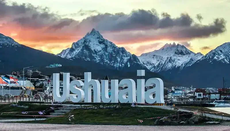 Ushuaia sign with snow-capped mountains at sunset in Tierra del Fuego, Argentina.