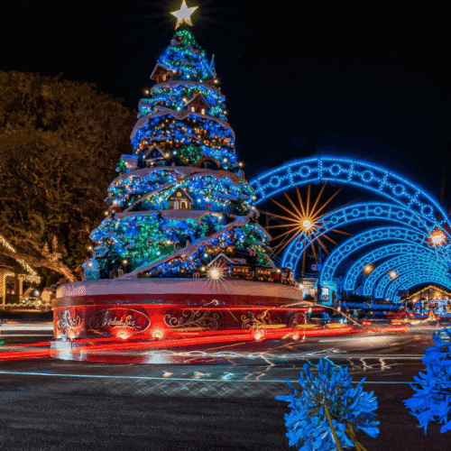 Árbol de Navidad decorado con luces azules y estrellas en una plaza festiva en la noche.