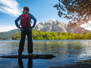 Hiker standing on a rock in a river with mountains and trees in the background.