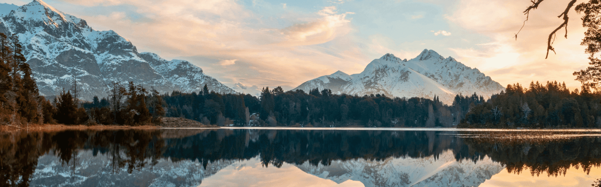 A scenic view of snow-capped mountains reflected in a calm lake at sunset, showcasing natural beauty.