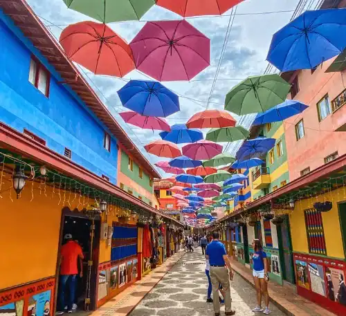 Colorful umbrellas hanging over a vibrant street with shops and pedestrians in a lively urban scene.