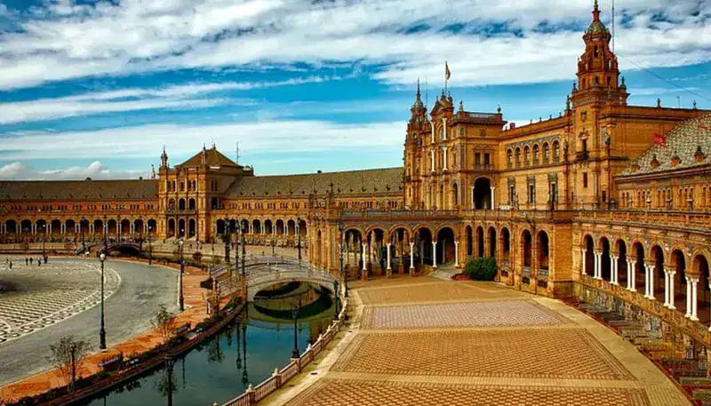 Historic building with arches and towers along a canal in Seville, Spain.