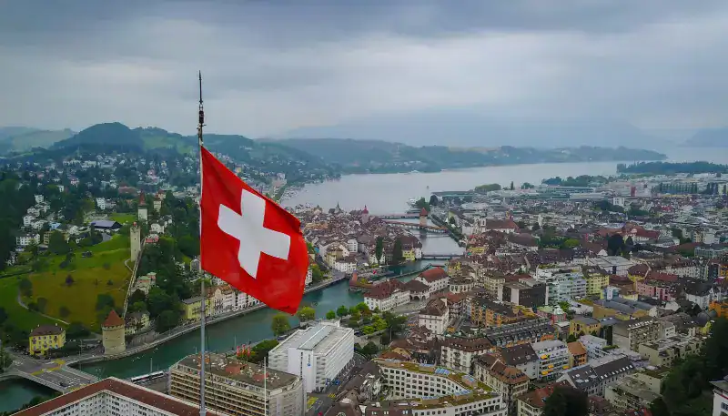 A lush aerial view of Zurich with the Swiss flag prominently displayed in the foreground.