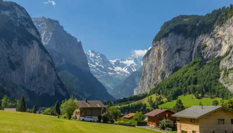 A lush green valley with charming houses surrounded by towering mountains and snow-capped peaks in t.